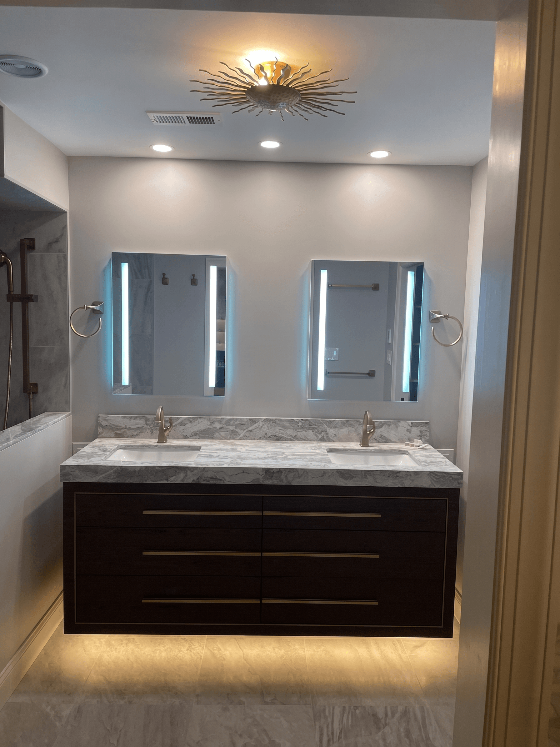 Completed master bathroom with full-height tile, frameless glass enclosure, brushed-brass fixtures, and custom mitered niche shelving.