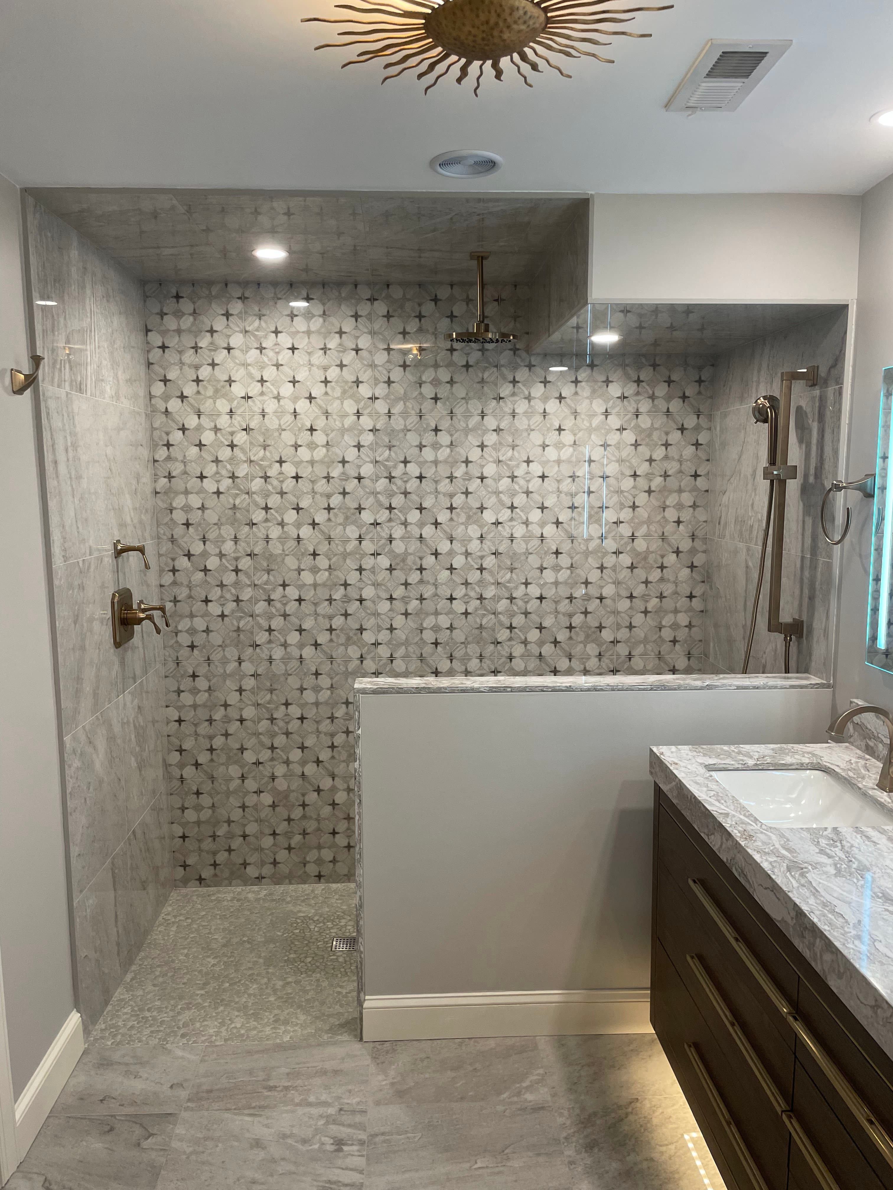 Completed secondary bathroom with patterned marble mosaic feature wall, recessed LED lighting, rainfall showerhead, and floating vanity with under-cabinet accent lighting.
